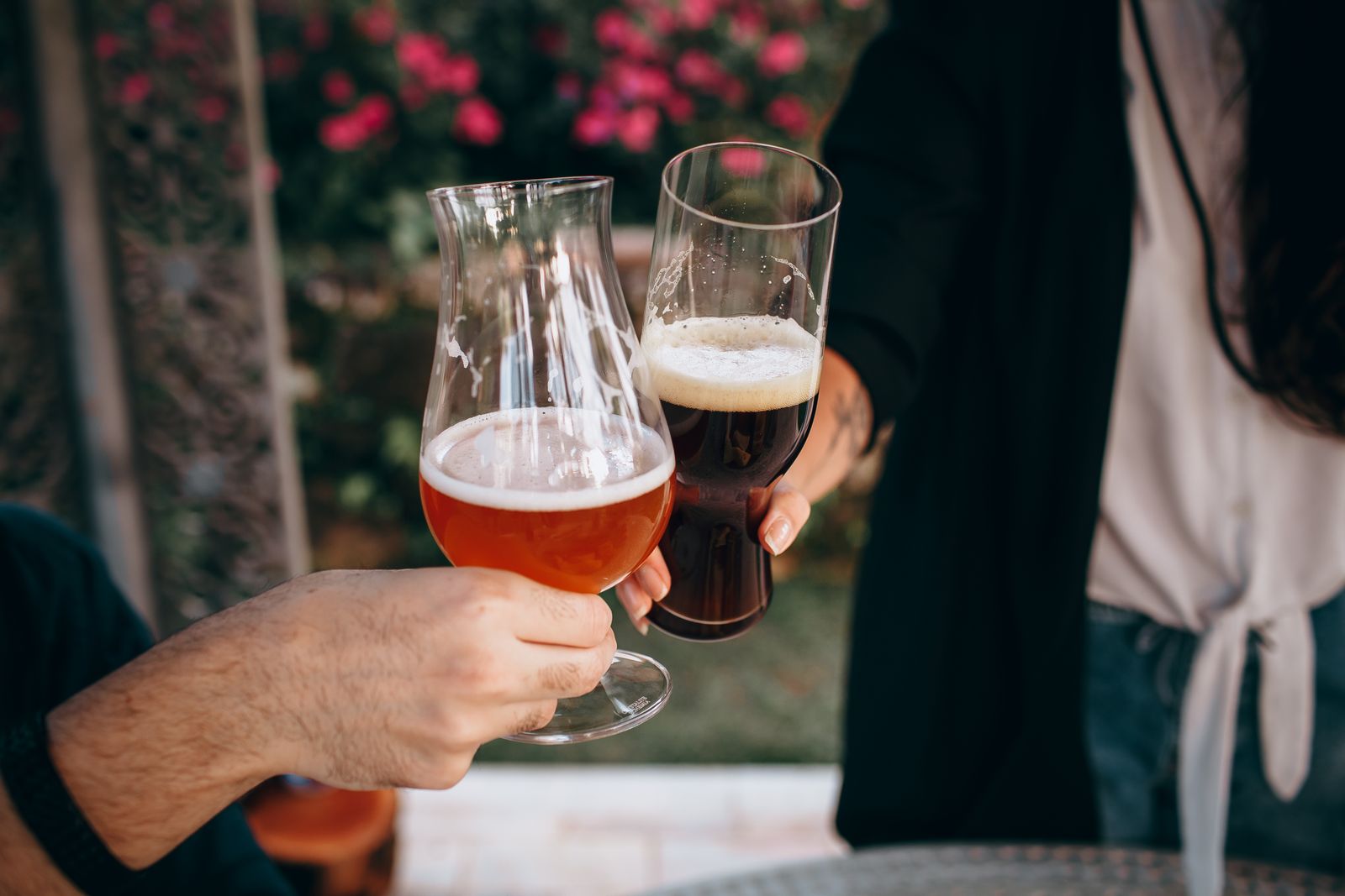 Two people clinking beer glasses outdoors on a sunny day