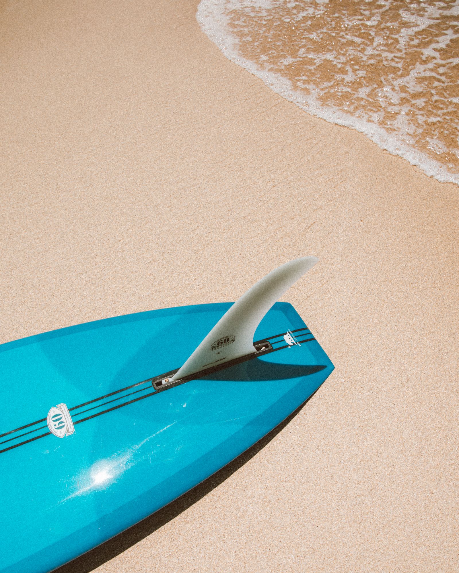 Blue surfboard resting on white sand beach