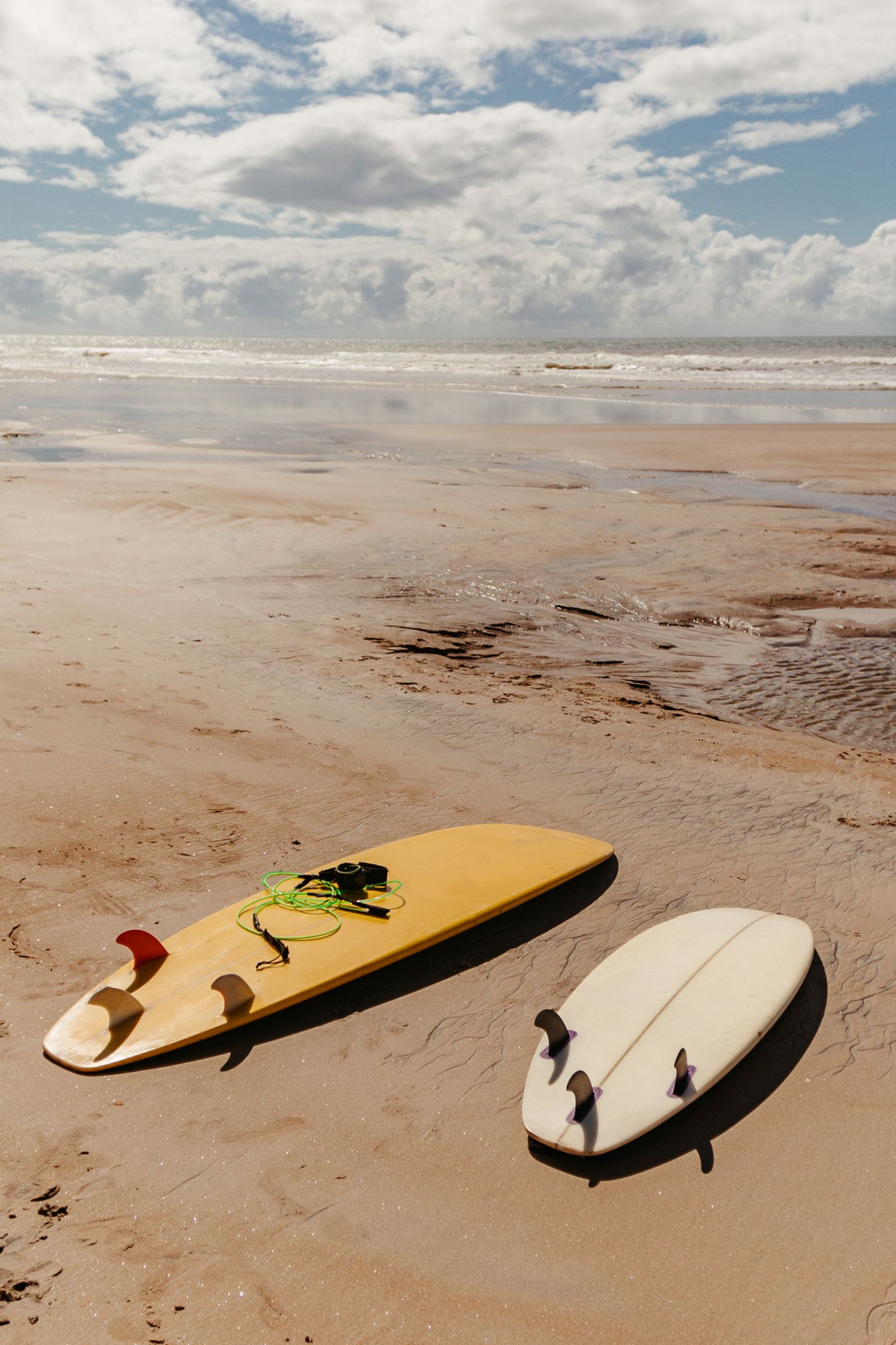 Two surfboards resting on a sandy beach under a bright sky